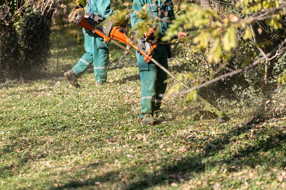 Men in green uniforms trimming grass