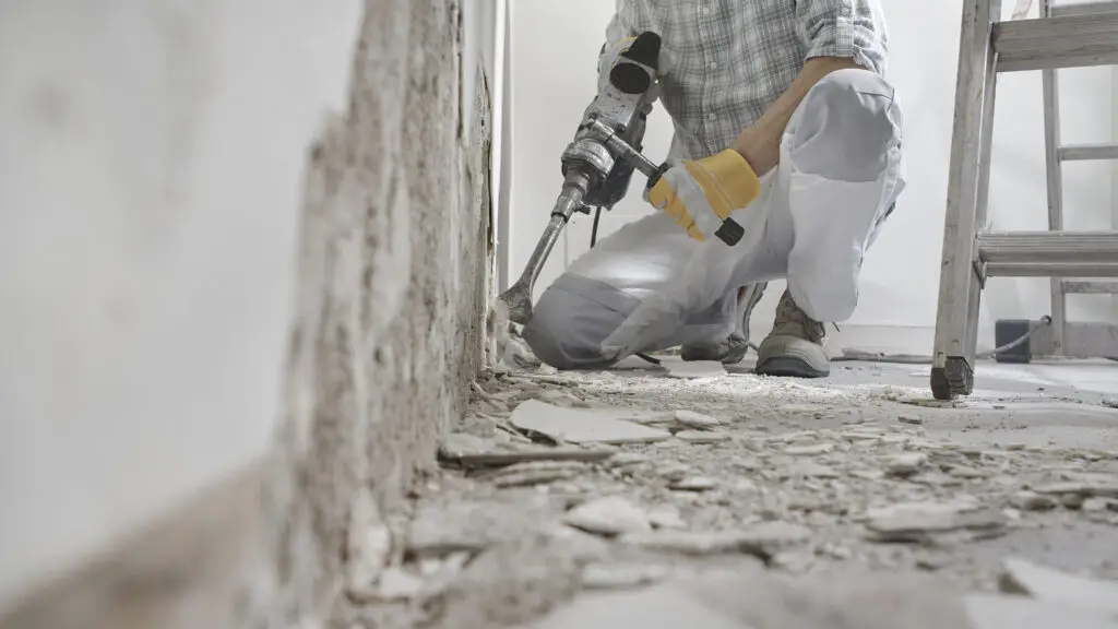 House renovation concept. Construction worker with protective gloves at work breaks the wall with the jackhammer after home services SEO filled their calendar with work.