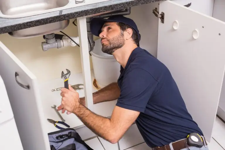 Plumber fixing under the sink after plumbing web design services created a site that filled their calendar with work.