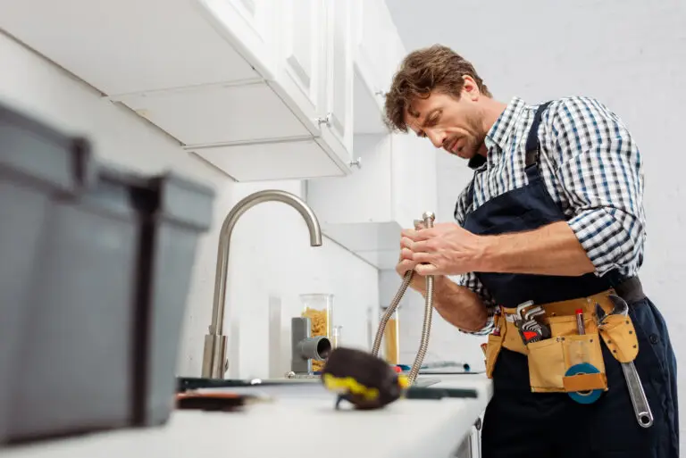 plumber holding metal pipe near kitchen faucet and tools on worktop after earning a job.