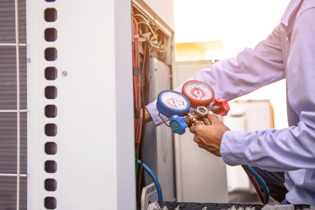 Technician using manifold gauge is measuring equipment for filling industrial factory air conditioners and checking maintenance outdoor air compressor unit after plumbing and HVAC SEO services filled their calendar with work.