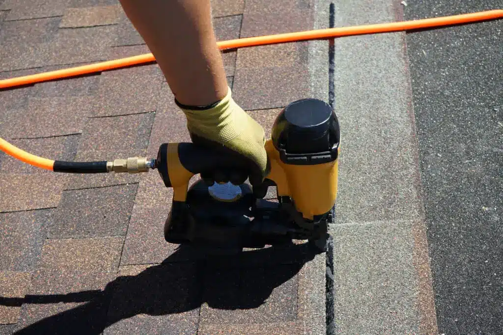 New roof shingle being applied. A Roofer nailing asphalt shingles with air gun after securing roofing leads.