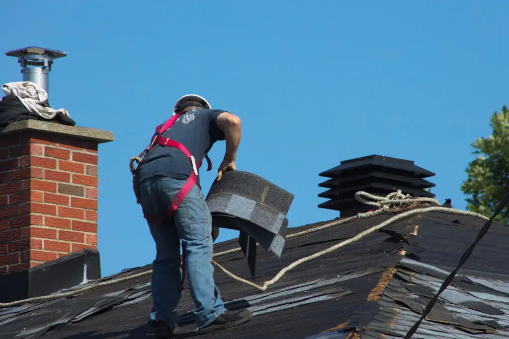 construction man roofer working on roof removing shingles repair after securing roofing leads.